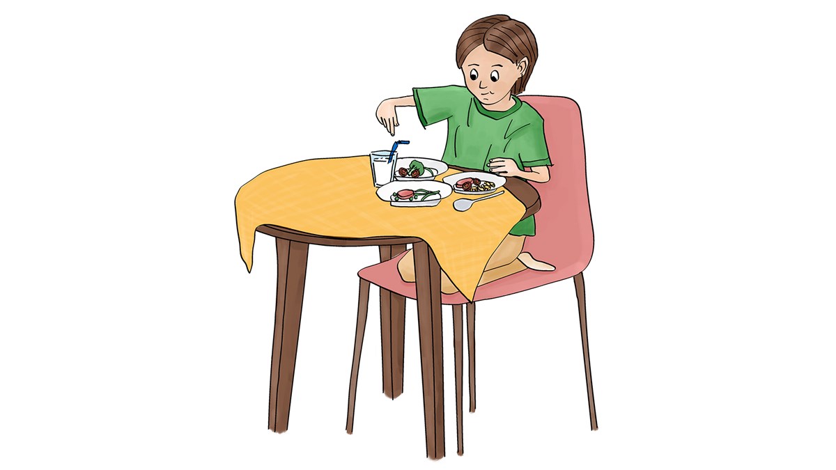 ett barn sitter på en stol vid ett bord. Barnet har tre tallrikar fram för sig på bordet och ett glas med ett sugrör i. 