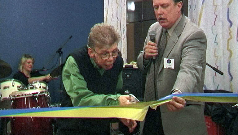 Jan Norinder holding holding an inauguration ribbon an another person cutting it.
