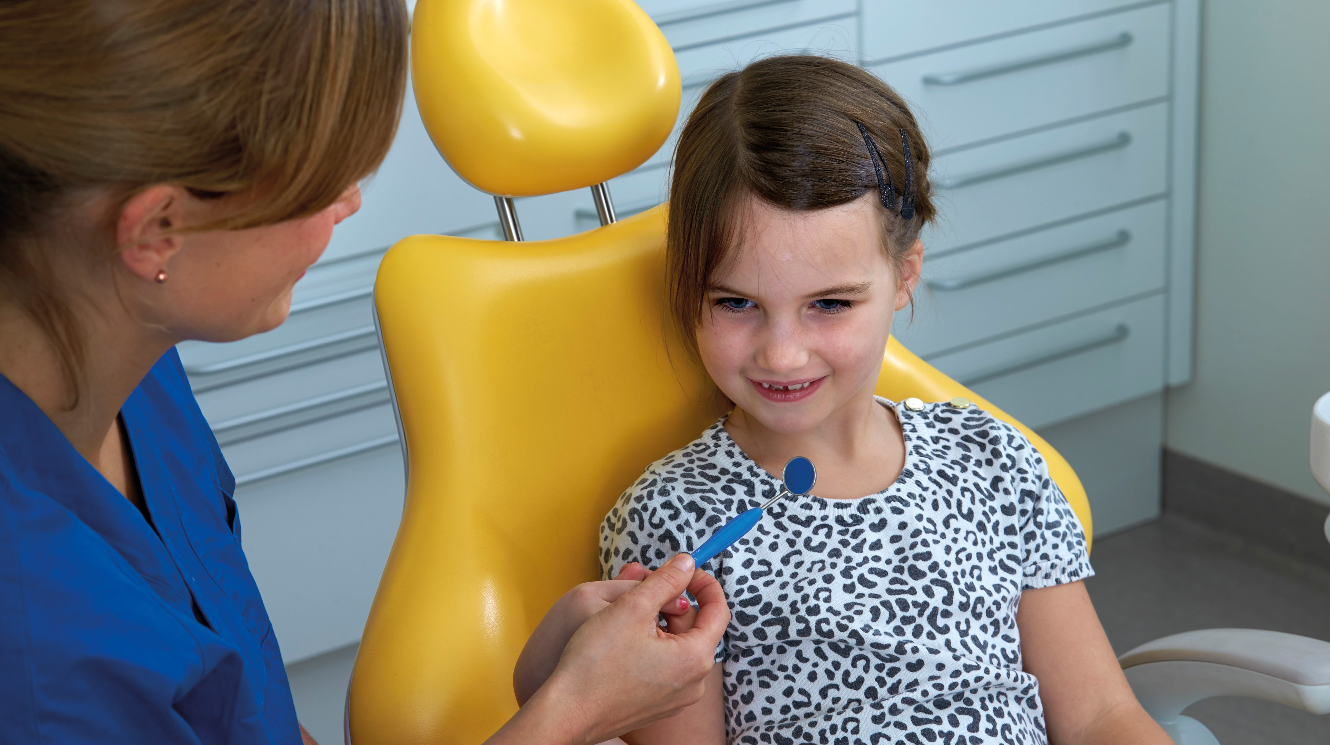 Ett barn i behandlingsstolen och en behandlare bredvid som visar en spegel.