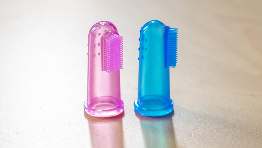 Två fingerborstar. Den vänstra i rosa, den högra i blå. Båda genomskinliga som man sätter på fingret. De har borstar på halva sidan.